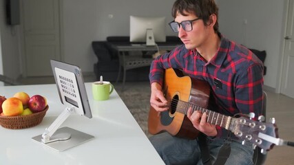 Educational showing guitar chord techniques at home, man in glasses teaching guitar chords at home at tablet. Vlog-style setup for online lessons or music tutorials, acoustic guitar in relaxed setting