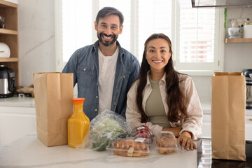 Portrait of happy spouses stand in domestic kitchen at counter with products ordered through website or purchased at market, feel satisfied, cooking together on weekend at home, fresh, homemade food