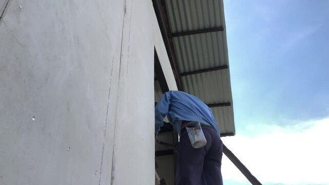 construction worker is installing fiber cement board using a hammer on a small wooden farmhouse.