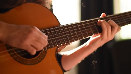 A person's hands skillfully play a musical instrument, creating beautiful melodies with the strings of a wooden guitar.