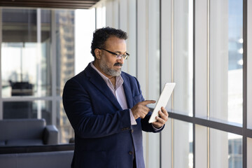 Senior Indian business professional executive man in formal jacket using Internet technology,...