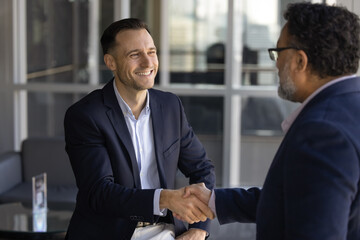 Happy successful financial consultant man shaking hands with older Indian male client, sitting in...