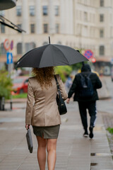 Woman with umbrella on wet city sidewalk, rainy day in urban environment, professional female...