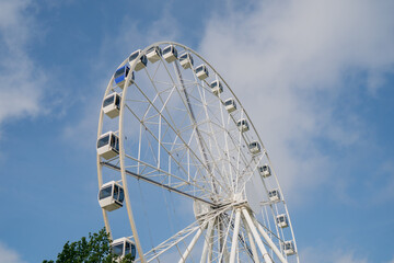 Giant white Ferris wheel rising into sky, amusement park ride with cabins, observation wheel for...
