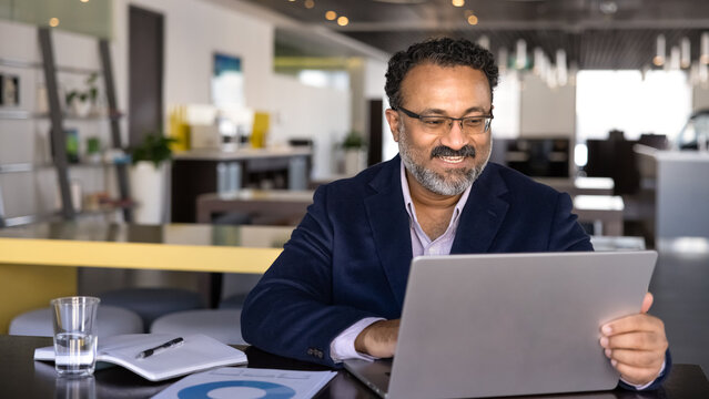 Positive successful senior Indian business professional man typing on laptop, using computer for communication in co-working hall, working on Internet ebusiness project. Banner shot