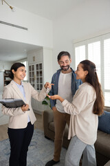 Young professional realtor woman hands over keys to pretty Latin spouses, stand in cozy living room, finalize meeting. Acquisition of new or secondary housing, property transaction, real-estate deal
