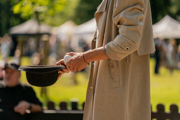 Street theater clown in light trench coat presenting black bowler hat, cropped closeup of costume...
