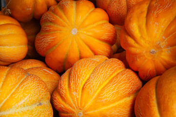A pile of bright yellow orange ribbed melons with prominent white veining. These unique textures and shapes make the image ideal for autumn harvest, organic farming, or rustic market visuals