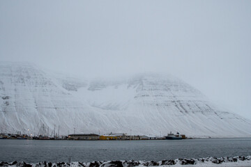 Foggy view of Ísafjörður harbor in Iceland, with snow-covered fjord mountains in the background....