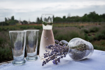 Sweaty jug of cool drink and mint leaves and glasses sits on a table covered with a tablecloth...