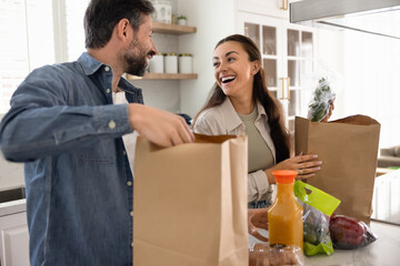 Pretty couple in love unpacking two paper grocery bags with purchased or ordered foodstuff, take...