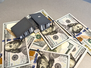 Small house r sitting on a stack of hundred dollar bills against white background. Concept of real...