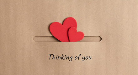 Two pink hearts emerging from a slot on a card with the message thinking of you written below it