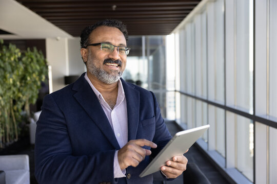 Happy pensive senior business executive man typing on digital tablet in office hall, looking away, smiling, thinking on online sales growth, successful financial trading, investment management - Powered by Adobe