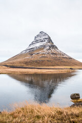Scenic view of Kirkjufell mountain in Iceland reflected in the calm waters of a lake on a cloudy,...