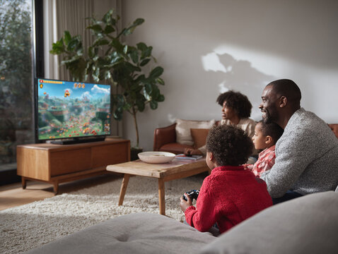 A loving family, including kids, joyfully play video games together on a TV in their cozy living room. A warm, modern scene showcasing leisure and connection.