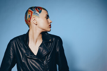 Young woman with colorful shaved hairstyle wearing black leather jacket looking sideways against...