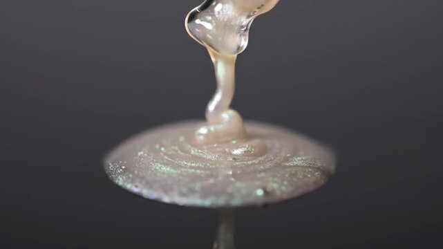A close up shot captures a translucent liquid droplet forming and falling against a dark, neutral background, showcasing its smooth texture.