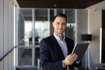 Positive confident young Hispanic CEO man posing for portrait with digital gadget in office hall,...
