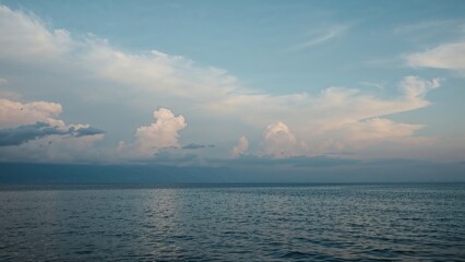 The horizon glows with gentle pastel hues while clouds float above a tranquil sea at dusk.