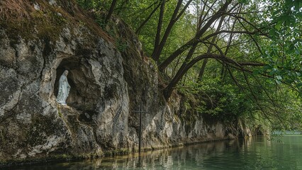 Fototapeta premium Sculpture of the Virgin Mary set inside a rocky grotto beside a river