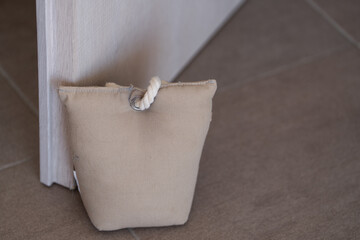 Small canvas bag filled with sand used as a doorstop, placed on the floor to keep a door open