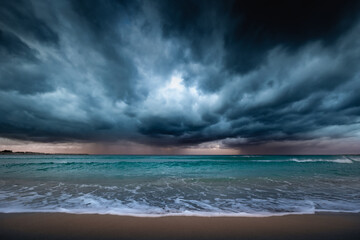Dark dramatic seascape stormy clouds, distant rain and waves crashing on sandy beach, Sicily, Italy