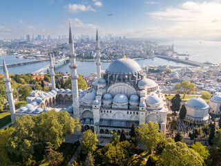 Big ancient mosque with four minarets in front of modern cityscape on sunny day, Istanbul, Türkiye