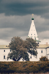 Ancient Russian whitewashed church on hill top among trees on cloudy day, Suzdal, Russia