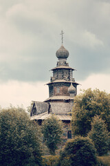 Ancient Russian wooden church on hill top among trees on cloudy day, Suzdal, Russia