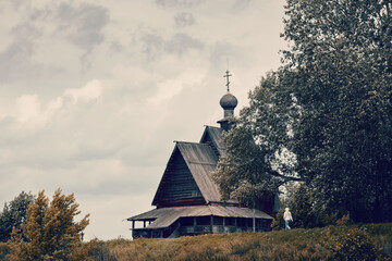 Ancient Russian wooden church on hill top among trees on cloudy day, Suzdal, Russia