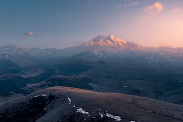 Landscape with snow-covered Mount Elbrus shining brightly in golden light of sunset, Caucasus, Russia