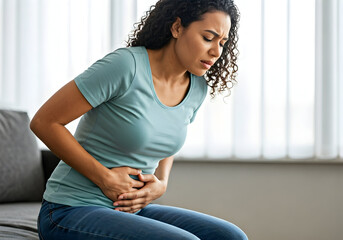 A young woman experiences abdominal pain likely period cramps or indigestion she sits clutching her stomach indoors suitable for health articles or medical content