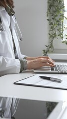 Doctor woman wearing white lab coat over green shirt, and stethoscope, is typing on laptop,...