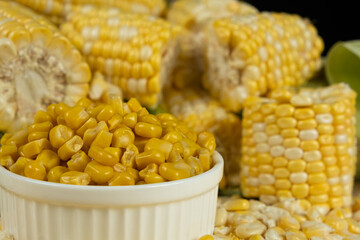 Bowl Of Preserved Corn Kernels With Fresh Corn Cobs Around.