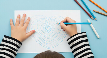 Child drawing heart shapes with a blue pencil on white paper with other pencils nearby on blue surface