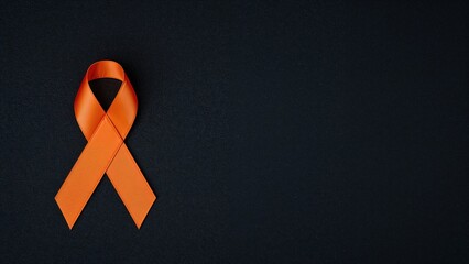 Top-down shot of an orange ribbon on a dark wooden background highlighting awareness for several diseases and diversity.