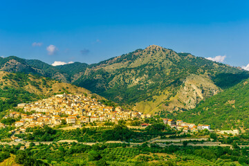 amazing mountain landscape with old yellow italian town among green beatiful mountains and cloudy sky above