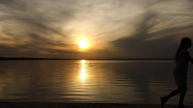 Two little sisters happily play paragon in front of the setting sun and the big lake. Beautiful sunset.