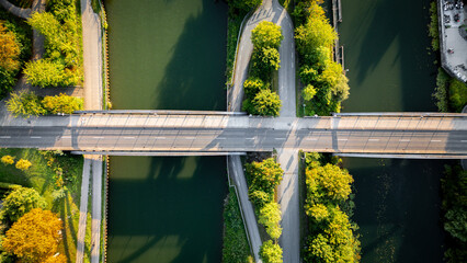 Aerial top-down view of a bridge crossing over a canal, with roads, pathways, and lush green trees...