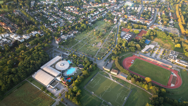 Aerial drone view of sports fields, stadium, and urban park surrounded by residential buildings in Germany.
