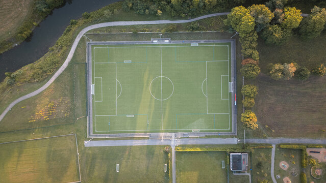 Aerial top-down view of a football field with green artificial turf and clear markings, sports infrastructure on a sunny summer day.