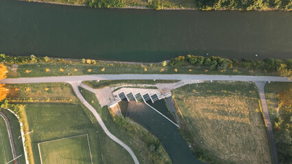 Aerial view of a canal with parallel paths, green vegetation and water obstacles, taken with a drone in warm morning light.