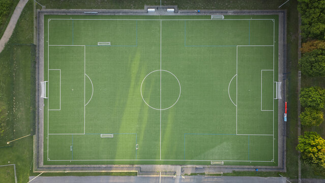 Aerial top-down view of a football field with green artificial turf and clear markings, sports infrastructure on a sunny summer day.