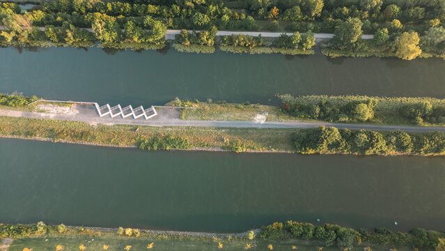 Aerial view of a canal with parallel paths, green vegetation and water obstacles, taken with a drone in warm morning light.