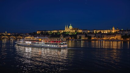 Fototapeta premium Blurred lights of a moving cruise ship against the backdrop of an ancient town at night, reflected in a river