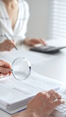 Two accountants are working together, using a magnifying glass and a calculator, to audit financial...