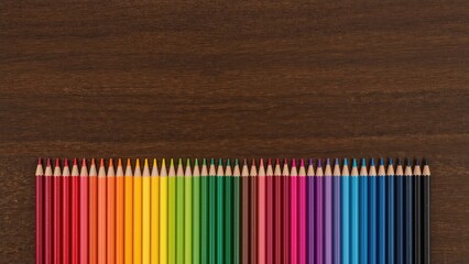 Obraz premium Wooden surface with colored pencils arranged to form a colorful rainbow