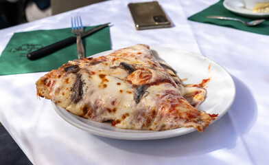 Thick slice of cheesy pizza with bacon and anchovies served on a white plate