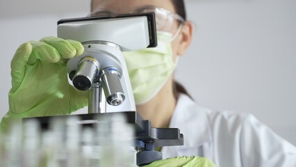 Close up of scientific precision involving green gloved hands adjusting microscope lens, blurred...